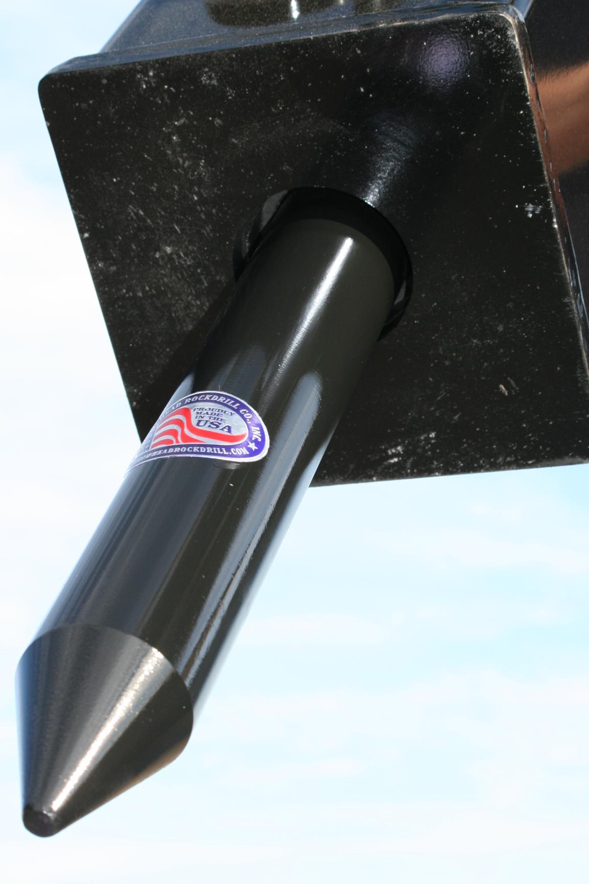 Side profile view of a conical moil point tool bit protruding from a hydraulic breaker bracket, with Arrowhead Rock Drill Co. Made in USA sticker visible