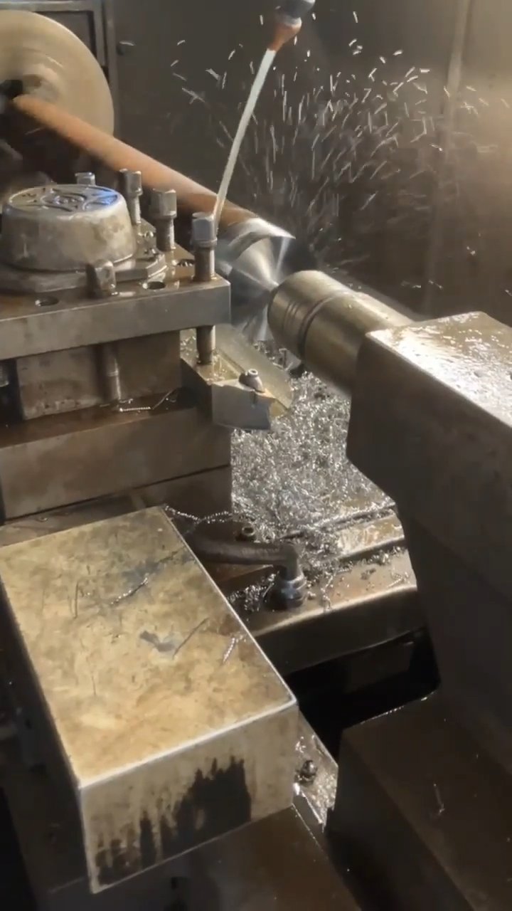 Close-up video of a CNC lathe machining a hydraulic breaker tool bit with coolant spray and flying metal chips