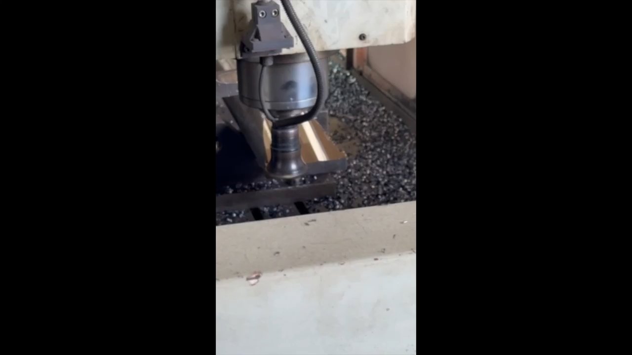 Close-up video of a hydraulic breaker tool bit being ground and finished on a machine with metal chips and coolant in a manufacturing shop