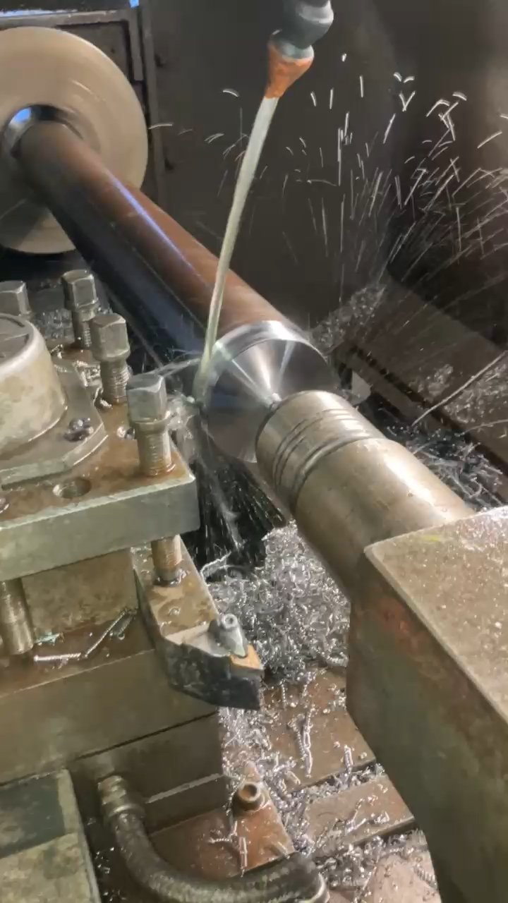 CNC lathe machining the conical taper tip of a hydraulic breaker tool bit with coolant spray and flying metal chips in a manufacturing shop