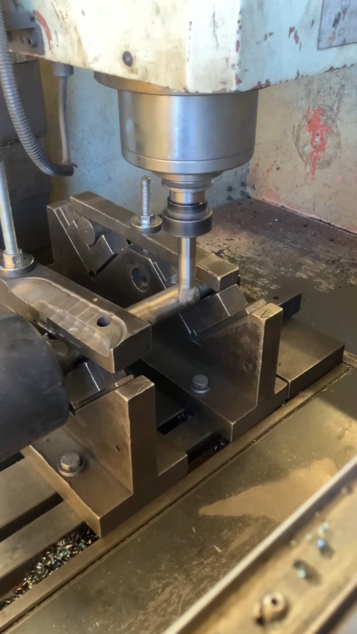 CNC milling machine drilling the retainer pin hole into a hydraulic breaker tool bit held in a precision clamping fixture